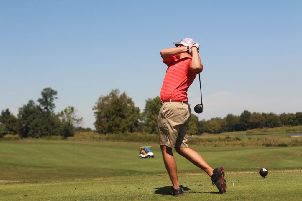 Man in red shirt and shorts finishing a golf swing